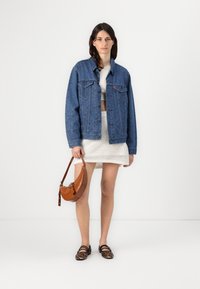 Denim jacket with a patterned texture, light blue color, cropped white knit top, white crochet skirt, brown shoulder bag, and leopard-print shoes.