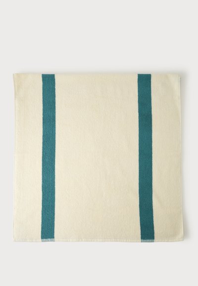 Serviette de couleur crème avec deux rayures verticales bleu sarcelle près de chaque bord, posée à plat sur un fond blanc.