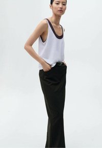 Witte tanktop met een donkere halslijn, gecombineerd met hoge zwarte broek. Glad materiaal en een ontspannen pasvorm gekenmerkt door een minimalistisch ontwerp.