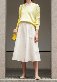 Żółty prążkowany sweter z dekoltem w serek, kremowa spódnica midi z dużymi kieszeniami, jasnobeżowe buty wsuwane oraz mała żółta torebka.