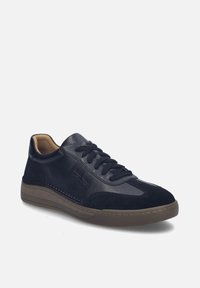 Baskets basses en cuir noir avec des accents en daim, laçage à l'avant, et semelle en caoutchouc marron inclinée vers la droite sur fond blanc.