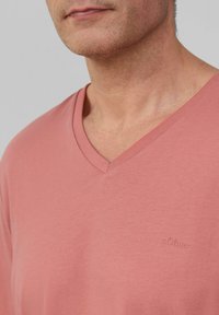 T-shirt w dekoltem w kształcie litery V w miękkim różowym kolorze z bawełny, z subtelnym logo s.Oliver i minimalną teksturą, podkreślająca swobodny, luźny krój.