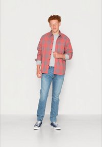 Ein kariertes Hemd in Rot und Grau über einem grauen Pullover, kombiniert mit blauen Jeans und marineblauen Sneakers. Gemütlicher Schnitt mit langen Ärmeln.