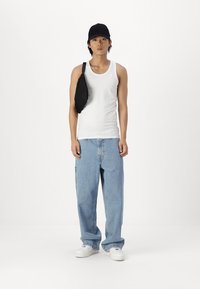 Hvit tanktopp, blå baggy jeans, svart caps og en svart skulderveske. Sneakersene er hvite med en teksturert overflate. En enkel, uformell antrekk.