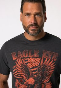 Zwarte t-shirt met grafisch ontwerp featuring een adelaar, Amerikaanse vlag, en de tekst "EAGLE EYE" in het rood. Korte mouwen, ronde halslijn, gemaakt van katoen.