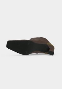 Bottine en daim marron avec semelle noire à bout carré et petit talon bloc, vue par dessous sur fond blanc.