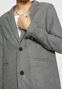 Grijze blazer van een wolmix met een reverskraag, sluiting met één knoop en twee voorzakken. Voorzien van zwarte knopen en een gestructureerde afwerking.