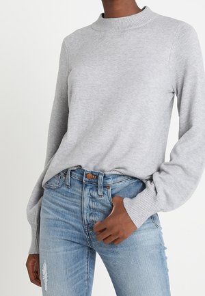 Pullover grigio con collo alto, maniche lunghe con polsini a coste, indossato sopra jeans in denim blu strappati.