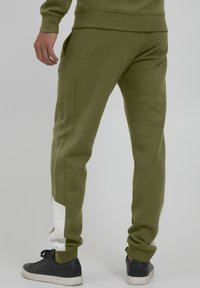 Olivgrüne Sweatpants mit schmalem Schnitt, ausgestattet mit einem weißen Akzent am unteren Bein, aus einem weichen, strukturierten Material; seitliche Taschen sichtbar.