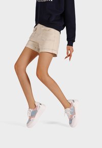 Sneakers con un design in materiali misti, con accenti rosa, blu e argento, montati su una suola bianca. Pantaloni corti beige casual e felpa blu navy.