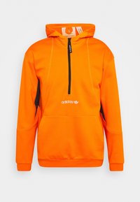 Orange hoodie med en kvart dragkedja, svarta sidopaneler och vit Adidas-logotyp fram. Tillverkad av ett mjukt, sträckbart material.