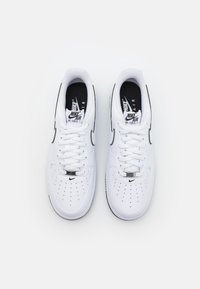 Fehér bőr Nike Air Force 1 sneakers fekete részletekkel, kerek orral, perforált kialakítással a légáteresztés érdekében, és lapos fehér fűzőkkel.