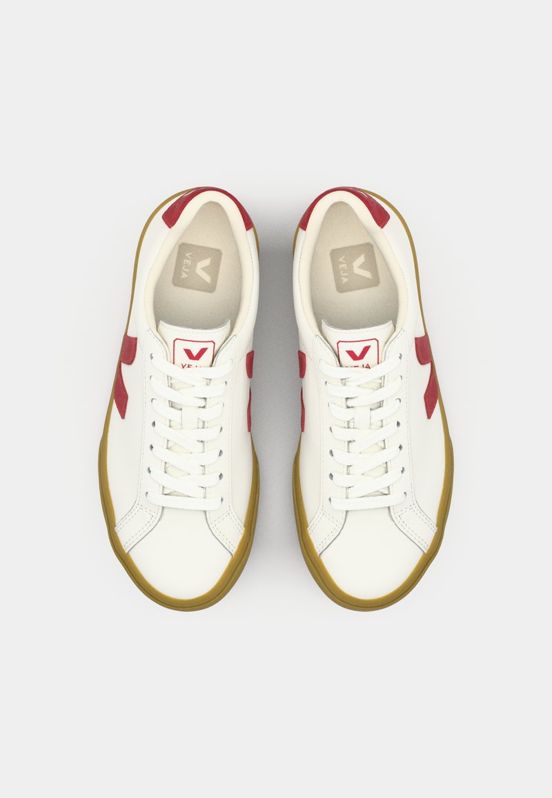 Sneakers bianchi con dettagli rossi e suola in gomma. Presentano un classico design con lacci. La soletta interna è di un grigio chiaro con marchio.