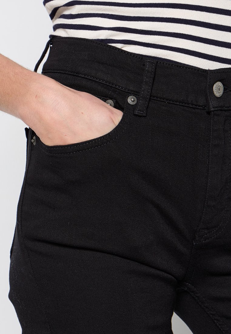 Schwarze Jeans aus Denim mit Fronttaschen, einem Reißverschluss und Metallknöpfen. Der Stoff hat eine glatte Textur und ein klassisches Schnittdesign.