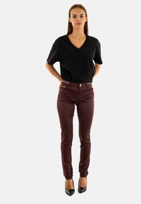 Top negro con escote en V y lunares blancos, combinado con pantalones ajustados burdeos que cuentan con un bolsillo lateral con cremallera, y zapatos de tacón negros puntiagudos.