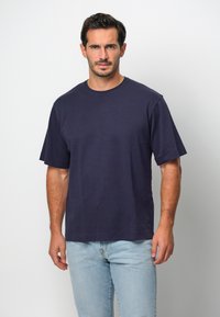 Marinblå t-shirt med kort ärm i bomull, med rund halsringning och en avslappnad passform, tillsammans med ljusblå jeans.