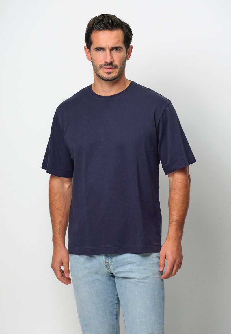 Marinblå t-shirt med kort ärm i bomull, med rund halsringning och en avslappnad passform, tillsammans med ljusblå jeans.