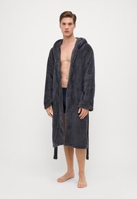 Grå, fluffy badekåpe med hette, lange ermer og knytelukking. Myk tekstur, kne-lengde, egnet for avslapning eller etter dusj.