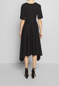 Svart midi klänning med korta ärmar, en figursydd bodice och en utsvängd kjol som faller längre bak. Kombinerad med svarta högklackade skor.