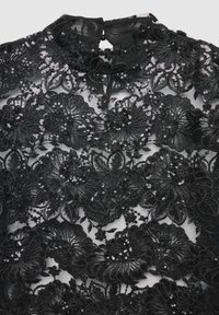 Top in pizzo nero con ricami floreali e paillettes, collo alto e apertura a chiave sulla schiena. Tessuto trasparente con motivi dettagliati.