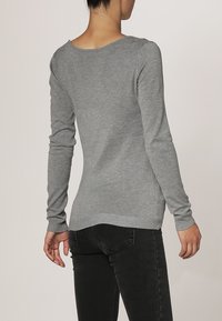 Pull gris à manches longues en tissu doux et extensible. Il présente un col rond et des poignets côtelés, conçu avec une coupe ajustée.