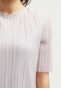 Haut plissé rose clair à manches courtes, texture douce, col rond et éclat discret pour une finition élégante.