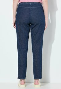 Tmavě modré džíny s rovnými nohavicemi, elastickým pasem a lemovanými manžetami. Tkanina vypadá hladce s jemnou strukturou.