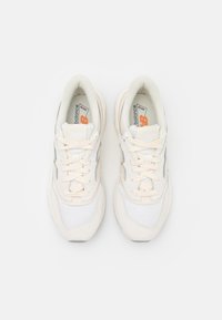 Fehér hálós és velúr sneakers, krémszínű fűzővel, ívelt dizájnnal, szürke részletekkel és narancssárga logóval a nyelvén.