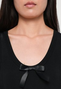 Must mustriga top ümmarguse kaelusega, millel on keskel väike must satiinist pael. Sile tekstuur ja keha lähedal disain.