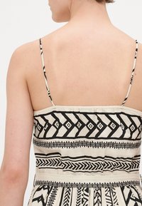 Rochie de vară fără bretele cu un fundal crem și modele geometrice negre îndrăznețe, țesătură texturată și un elastic la talie pentru o formă ajustată.