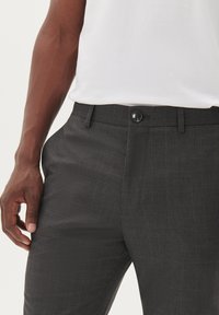 Pantalones de cuadros grises con una textura suave, que presentan un cierre de botón y bolsillos. El diseño incluye líneas de acento azul sutiles.