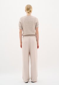 Beige pletený top s krátkým rukávem, texturovaný vzor a žebrované manžety, spárovaný s světle béžovými širokými kalhotami, obojí stylizováno jednoduše.