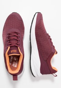 Pair of maroon athletic shoes with orange interior lining, white midsoles, and black outsoles, one shoe facing forward and the other sideways.