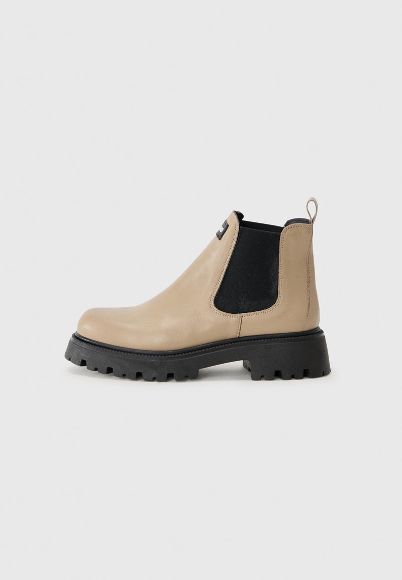 Bota Chelsea de couro bege com painéis laterais elásticos pretos, laço de puxar e sola de borracha preta grossa com padrão de relevos.