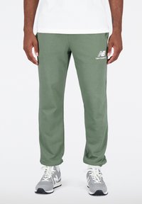 Zelené tepláky s měkkou texturou, elastickým pasem a bočními kapsami. Na horní části stehna je bílý logo. Nosit s šedými teniskami.