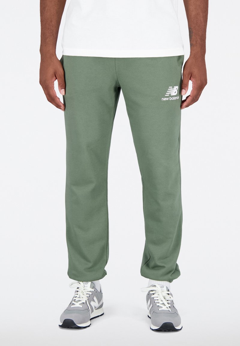 Zelené tepláky s měkkou texturou, elastickým pasem a bočními kapsami. Na horní části stehna je bílý logo. Nosit s šedými teniskami.