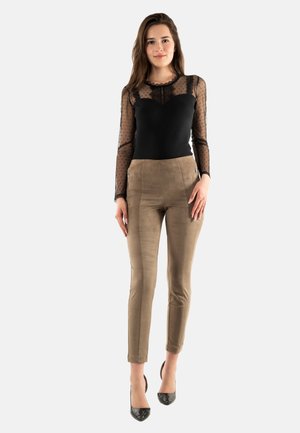 Parte superior negra de manga larga con mangas de lunares transparentes; pantalones slim ajustados color topo con cremalleras laterales; tacones altos negros brillantes.
