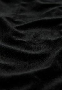 Black fabric with a soft texture, featuring prominent wrinkles and a smooth surface. Rich color depth enhances the appearance of folds.