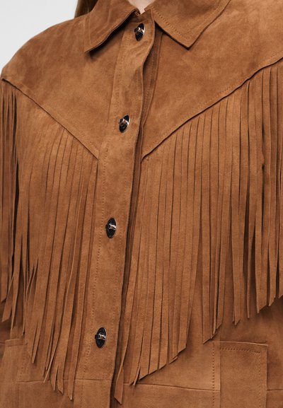 Καφέ καπιτονέ σακάκι από δέρμα σουέτ με μακριές φούντες στο στήθος και τα μανίκια, ασημί κουμπιά με πιαστρού και μυτερό γιακά.