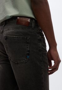 Dunkelgraue Jeans aus Denim mit einem braunen Lederpatch, blauer Nahtakzent auf der Gesäßtasche und einer taillierten Passform.