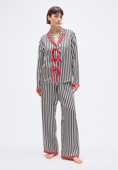 Set de pijamale cu dungi alb-negru și accente roșii, având un top cu nasturi și guler, împodobit cu fundițe decorative, și pantaloni cu picioare largi.
