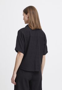 Camicetta nera a maniche corte in un tessuto leggero, con una vestibilità comoda, dettaglio dello yoke sul retro e orlo curvo.