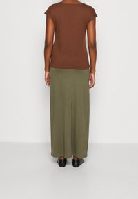 Top marrón de manga corta combinado con una larga falda verde oliva, ambas de tela suave. Presenta un corte holgado y un diseño sencillo. Zapatos negros.
