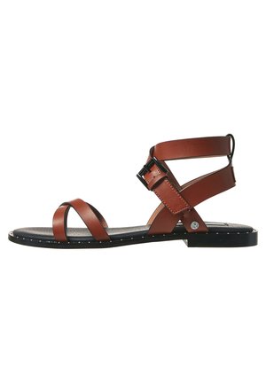 Brun læder flad sandal med sort sål, justerbar ankelrem med spænde og to krydsende remme foran på hvid baggrund.