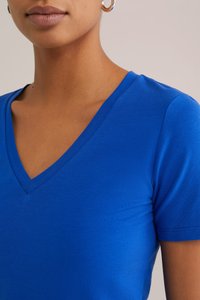 T-shirt bleu à col en V fabriqué en tissu doux, avec des manches courtes et un design ajusté, mettant en valeur une texture lisse et des détails de couture soignés.