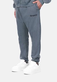 Pantalons de jogging gris avec des poignets élastiques, des poches latérales et "Dropsize" brodé en noir. Assortis avec des baskets blanches à semelle texturée.
