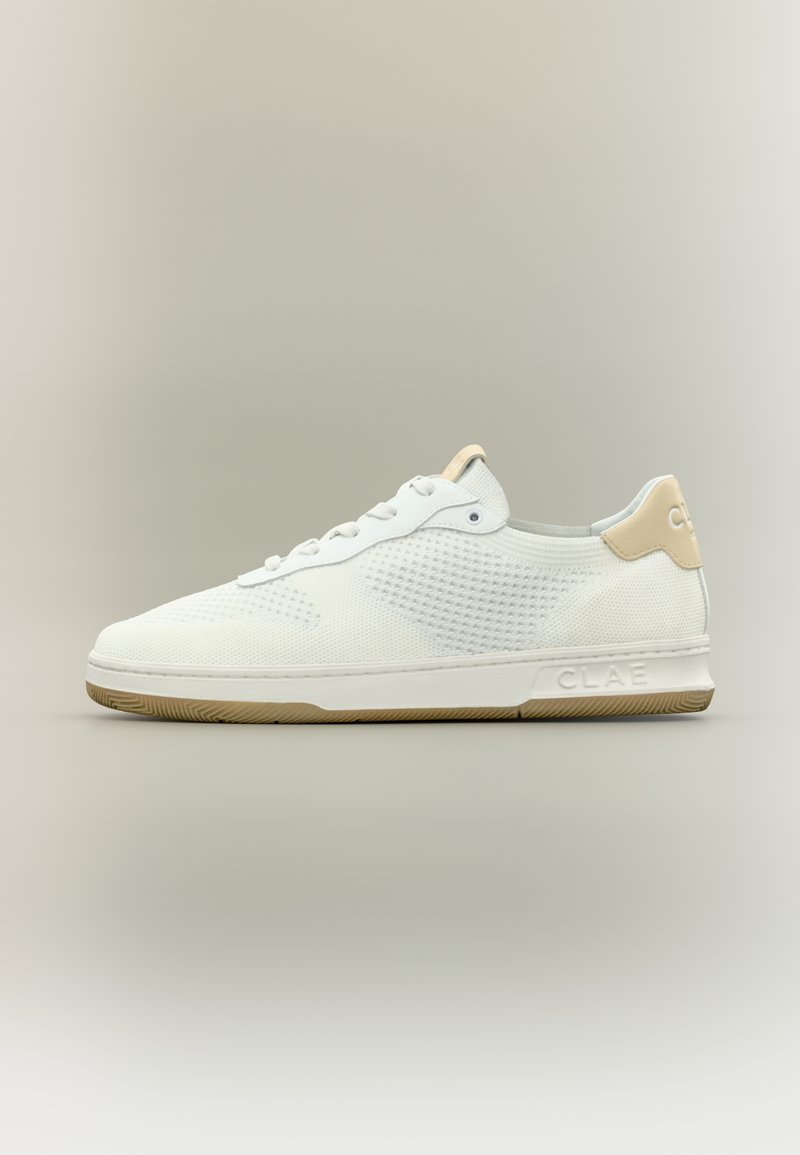 Λευκό χαμηλό αθλητικό παπούτσι με υφασμάτινη υφή, κορδόνια μπροστά, ταμπέλα φτέρνας σε μπεζ χρώμα και μπεζ σόλα, τοποθετημένο σε ουδέτερο φόντο.