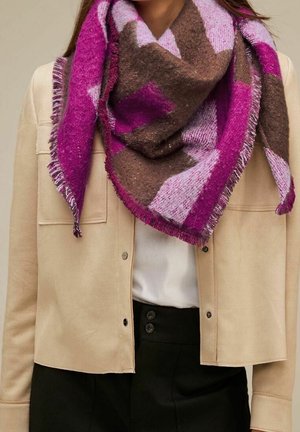 Écharpe en laine à motifs violets, marron et rose enroulée autour du cou, assortie à une veste beige à boutons, un haut blanc et un pantalon noir.