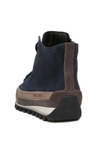 Bottine en daim bleu marine avec des accents en cuir brun, semelle en caoutchouc texturée et languette à l'arrière. Nom de la marque "Candice Cooper" visible.