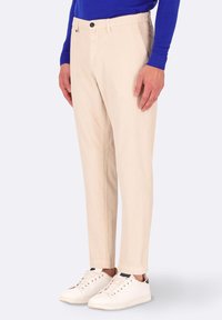 Pantaloni a strisce beige con una vestibilità affusolata, dotati di chiusura con bottone nero, tasche anteriori e abbinati a sneaker bianche.